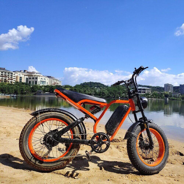 Boombike Bluvall SU8 moped ebike with 1500W motor parked on a sandy shore with a lake and buildings in the background.